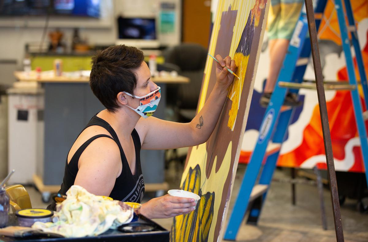 An art student wears a face covering while painting a class project.